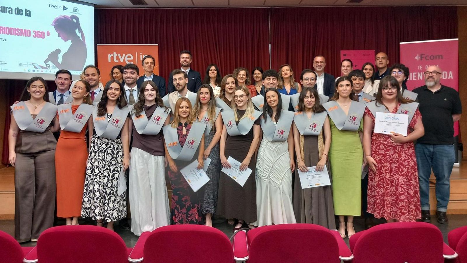 Graduación del Máster de Periodismo 360º de la UCM, con jóvenes portando diplomas y estolas grises, rodeados de profesores y banners de RTVE y la Facultad de Ciencias de la Información.