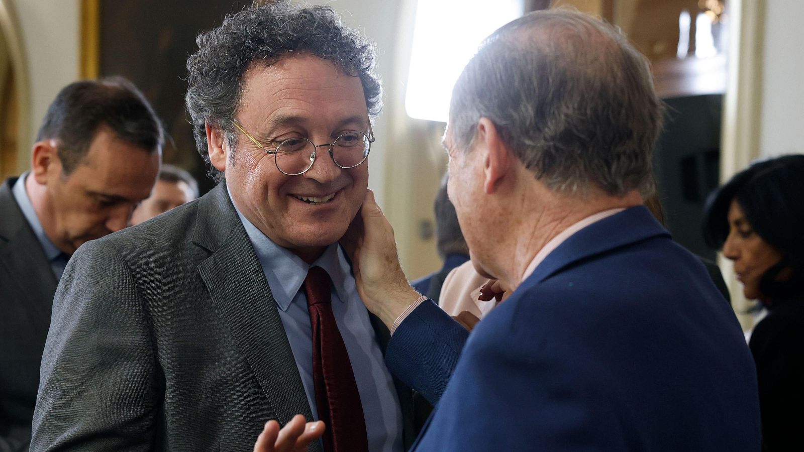 Álvaro García Ortiz, ex fiscal General del Estado, sonríe mientras un hombre le toca la mejilla en un evento.
