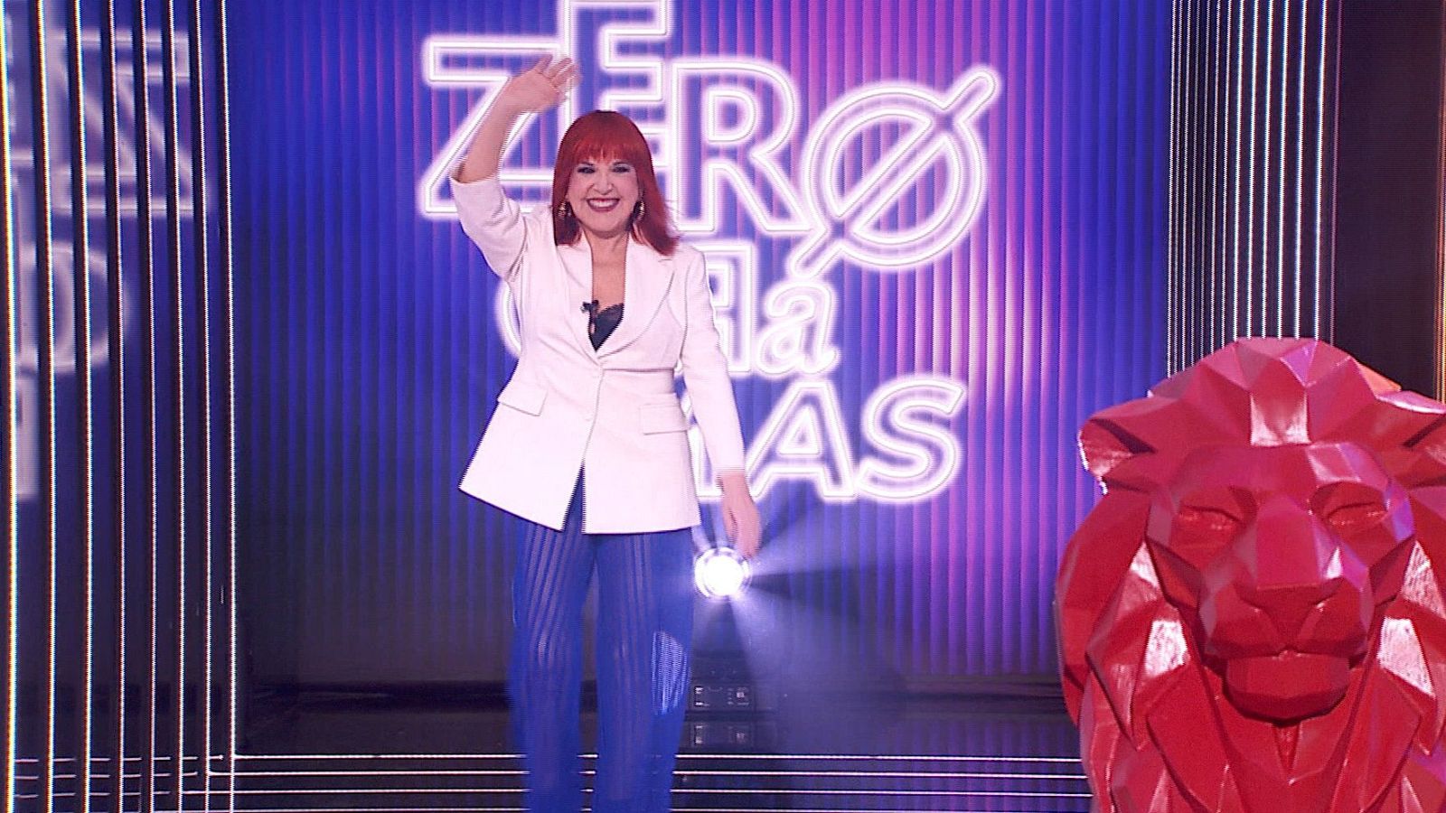 Loles León sonríe y saluda en un plató con letrero "ZERO Ø LA MÁS" y escultura de león rojo.