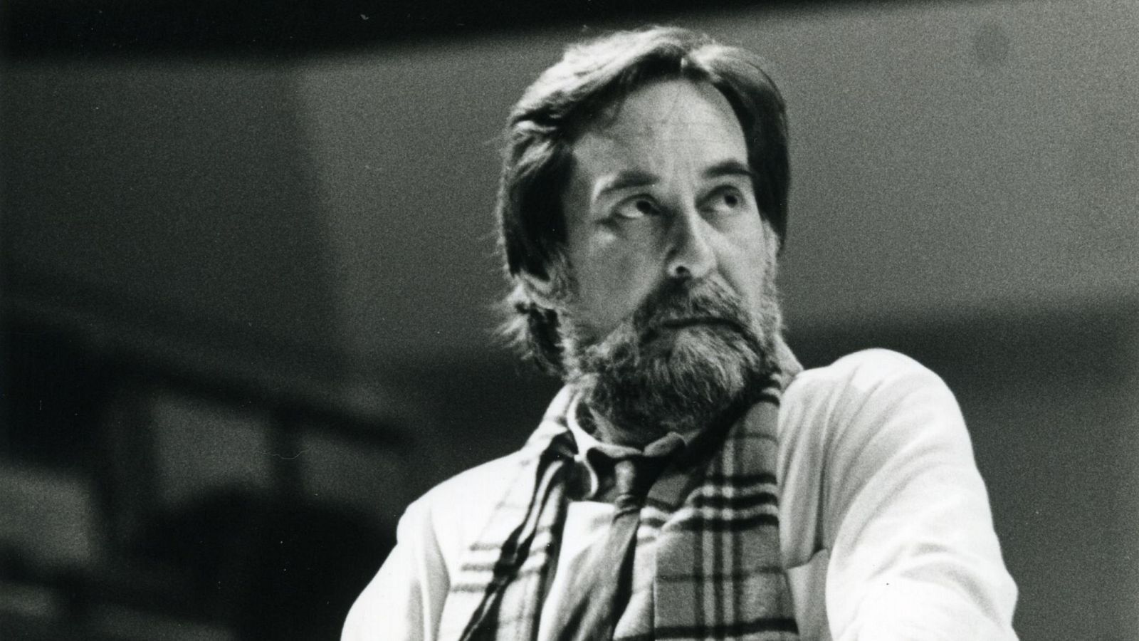 Rafael Taibo, actor español, en un retrato en blanco y negro. Cabello peinado hacia atrás con canas, barba cuidada, camisa clara y bufanda a cuadros. Fondo oscuro.
