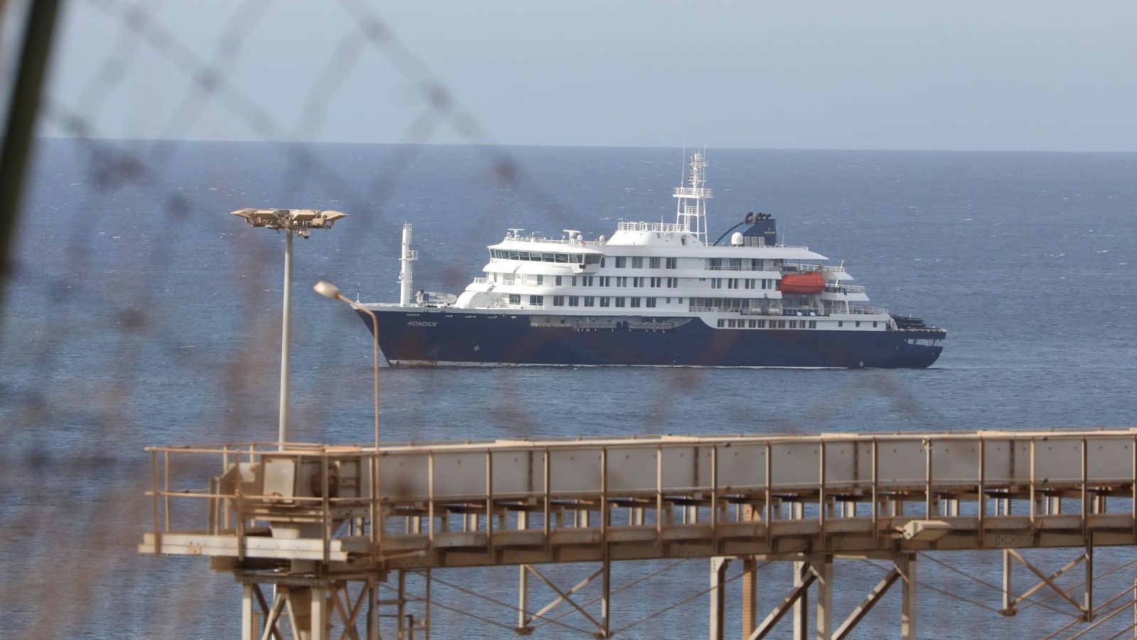 Crucero MV Hondius en aguas abiertas, con el nombre visible en la proa. Visto a través de una valla metálica en primer plano.