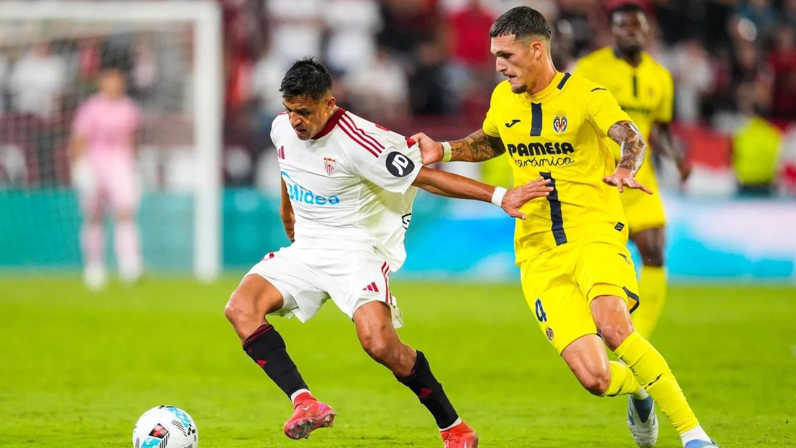 Alexis Sánchez (Sevilla) y Rafa Marín (Villarreal) luchan por el balón en un partido de fútbol. Sánchez viste camiseta blanca con detalles rojos, Marín de amarillo. El balón está en el césped. Fondo desenfocado con portería y gradas.