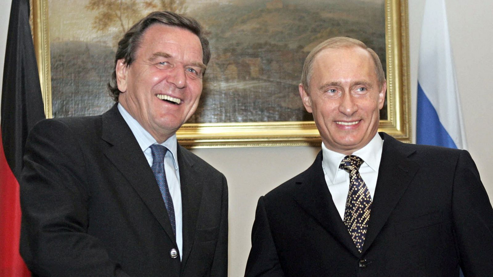 Gerhard Schröder y Vladimir Putin sonríen en un encuentro oficial, con las banderas de Alemania y Rusia al fondo.