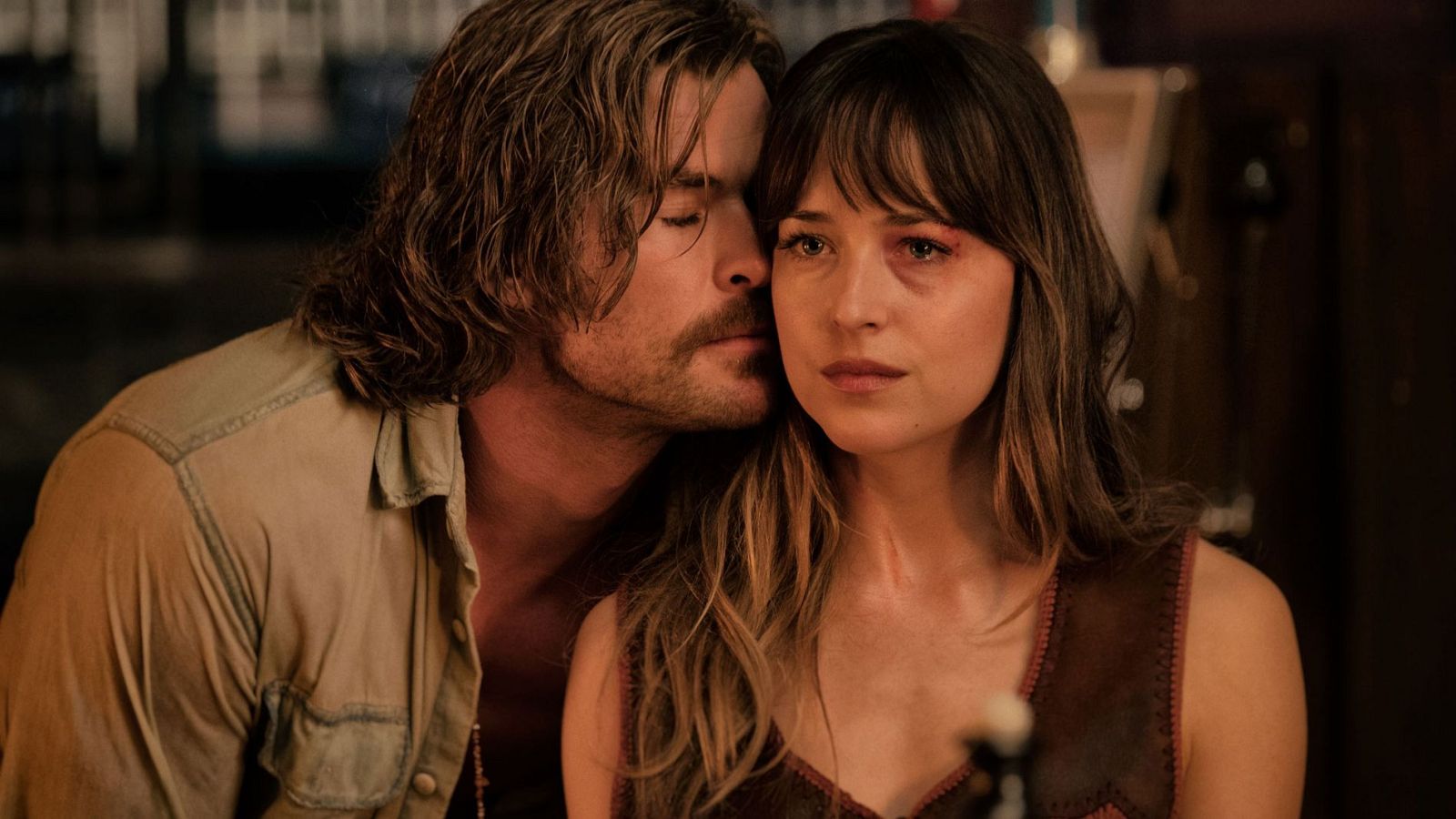Chris Hemsworth y Dakota Johnson comparten un momento íntimo y emotivo, con Hemsworth susurrando o consolando a Johnson, quien muestra una expresión seria y una marca en el rostro.