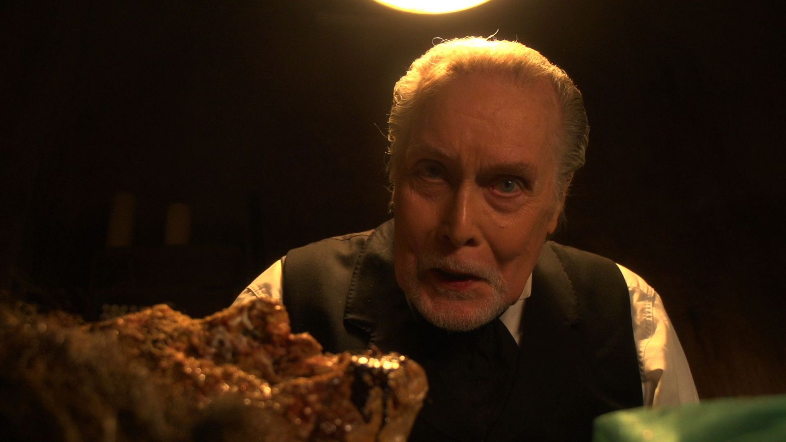 Jack Taylor, actor de piel clara y barba blanca, luce una expresión intensa con boca entreabierta. Un objeto grotesco y rojizo aparece desenfocado en primer plano.