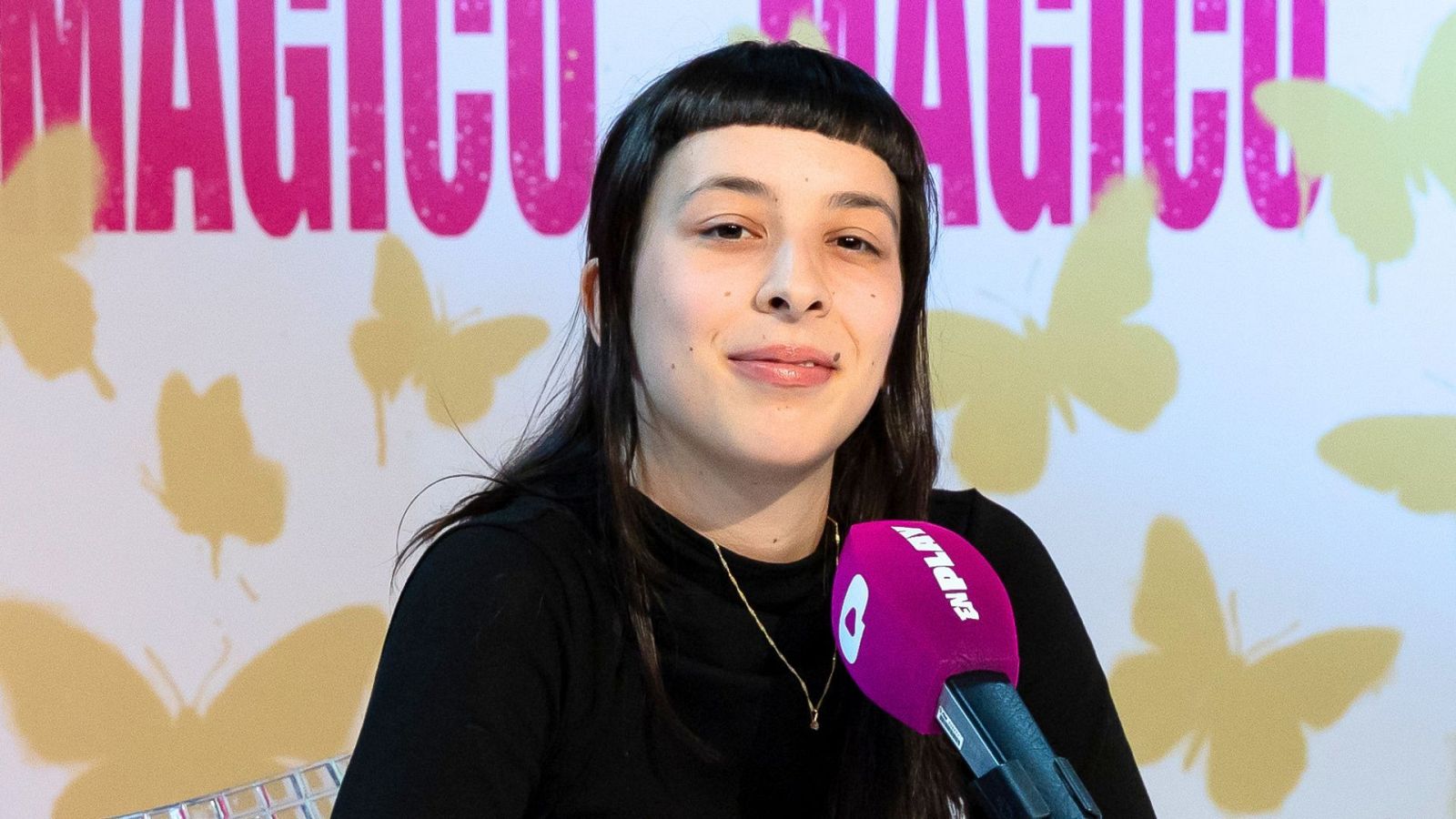 Primer plano de Marina Garcia Canedo con micrófono "EN PLAY" y fondo decorado con "MAGICO" y mariposas.