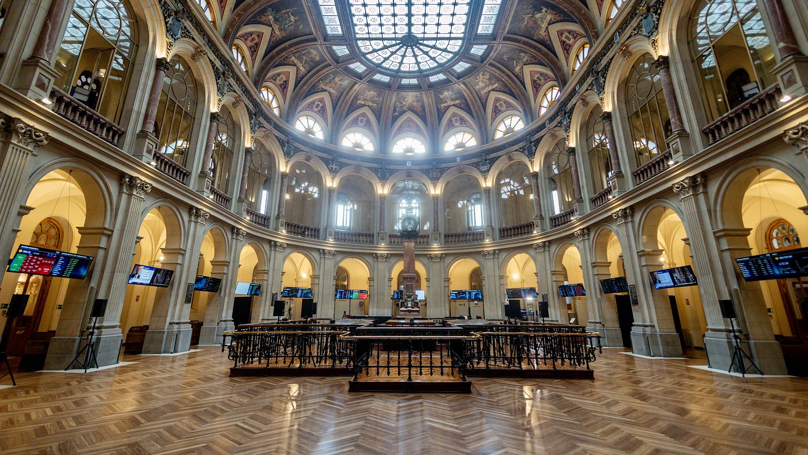 Impresionante interior del Palacio de la Bolsa de Madrid, con arquitectura clásica, cúpula de cristal y pantallas de datos financieros.