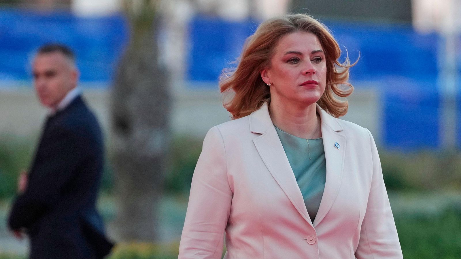 Evika Siliņa, Primera Ministra de Letonia, posa con chaqueta beige y blusa verde menta. Un hombre con traje oscuro la acompaña en el fondo desenfocado sobre un suelo rojizo.