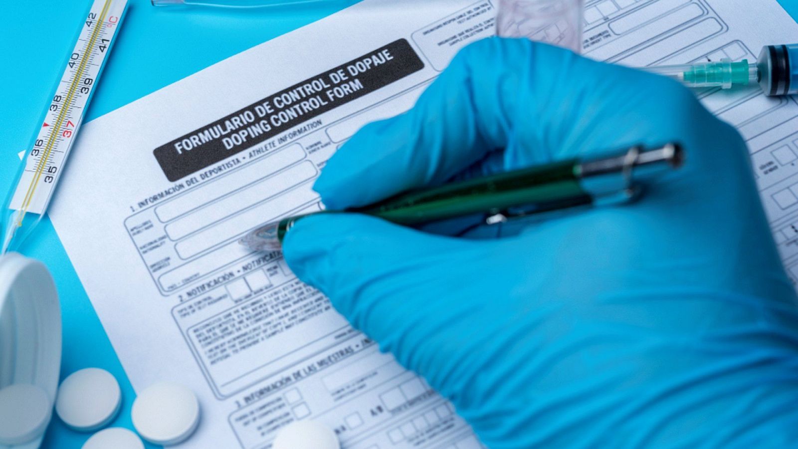Mano enguantada de azul escribe en formulario de control de dopaje bilingüe con termómetro, pastillas y jeringuilla. "FORMULARIO DE CONTROL DE DOPAJE / DOPING CONTROL FORM".