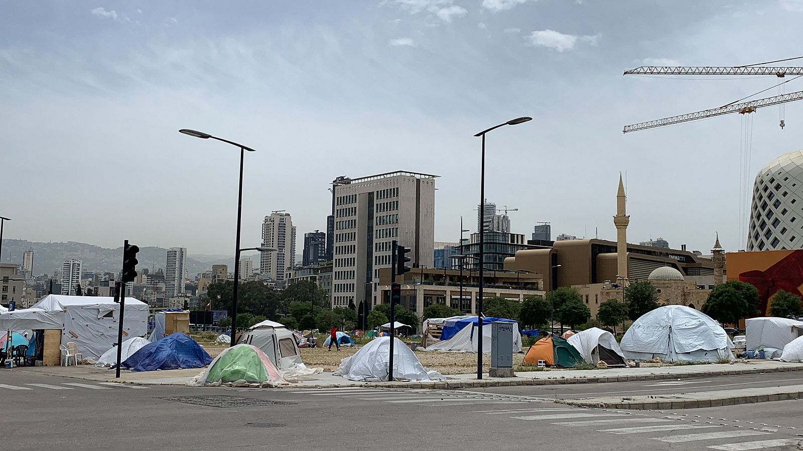 Campamento de tiendas de campaña para familias desplazadas en Beirut, Líbano, con edificios urbanos y grúas de construcción al fondo.
