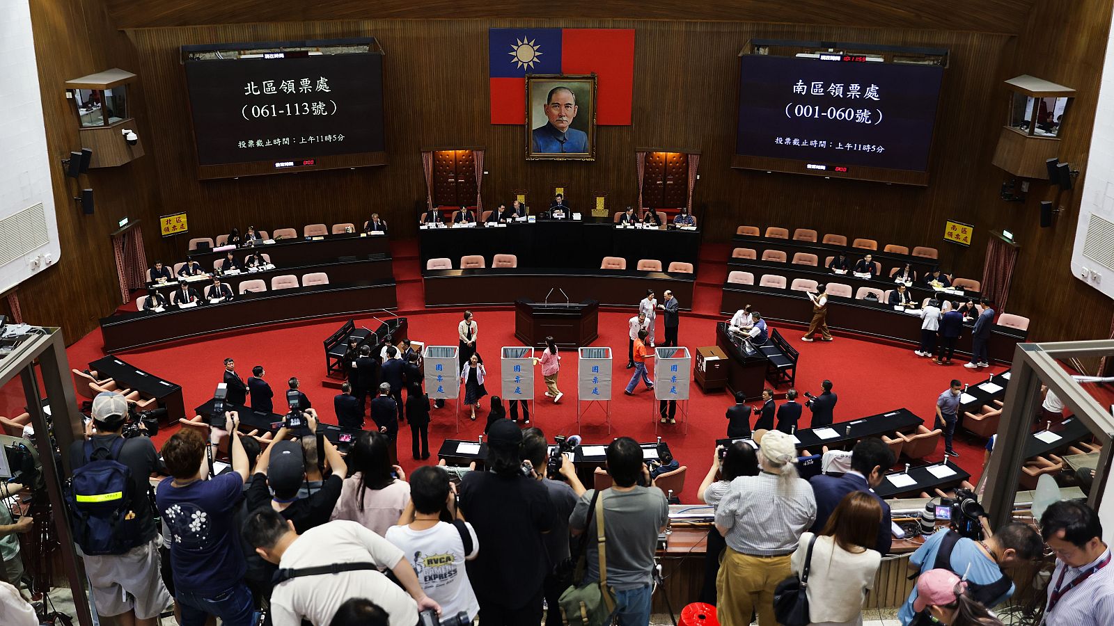 Vista del Parlamento de Taiwán durante una votación, con la bandera de la República de China y un retrato de Sun Yat-sen en el centro. Pantallas informan sobre los puestos de votación y la hora límite.