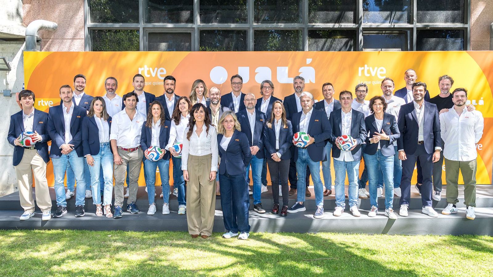Equipo de RTVE presenta la cobertura del Mundial 2026 con el lema "Ojalá". Elena Sánchez Caballero, María Eizaguirre y Arsenio Cañada entre los presentes. Balones de fútbol y cartel naranja de fondo.