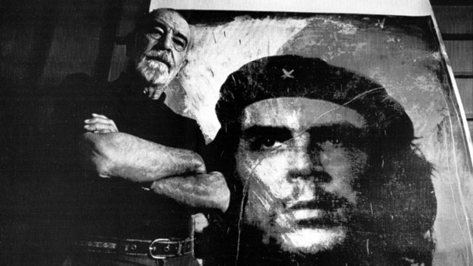 Alberto Korda, con barba canosa, posa con los brazos cruzados junto a una gran reproducción en blanco y negro de su famosa foto del Che Guevara, "Guerrillero Heroico".