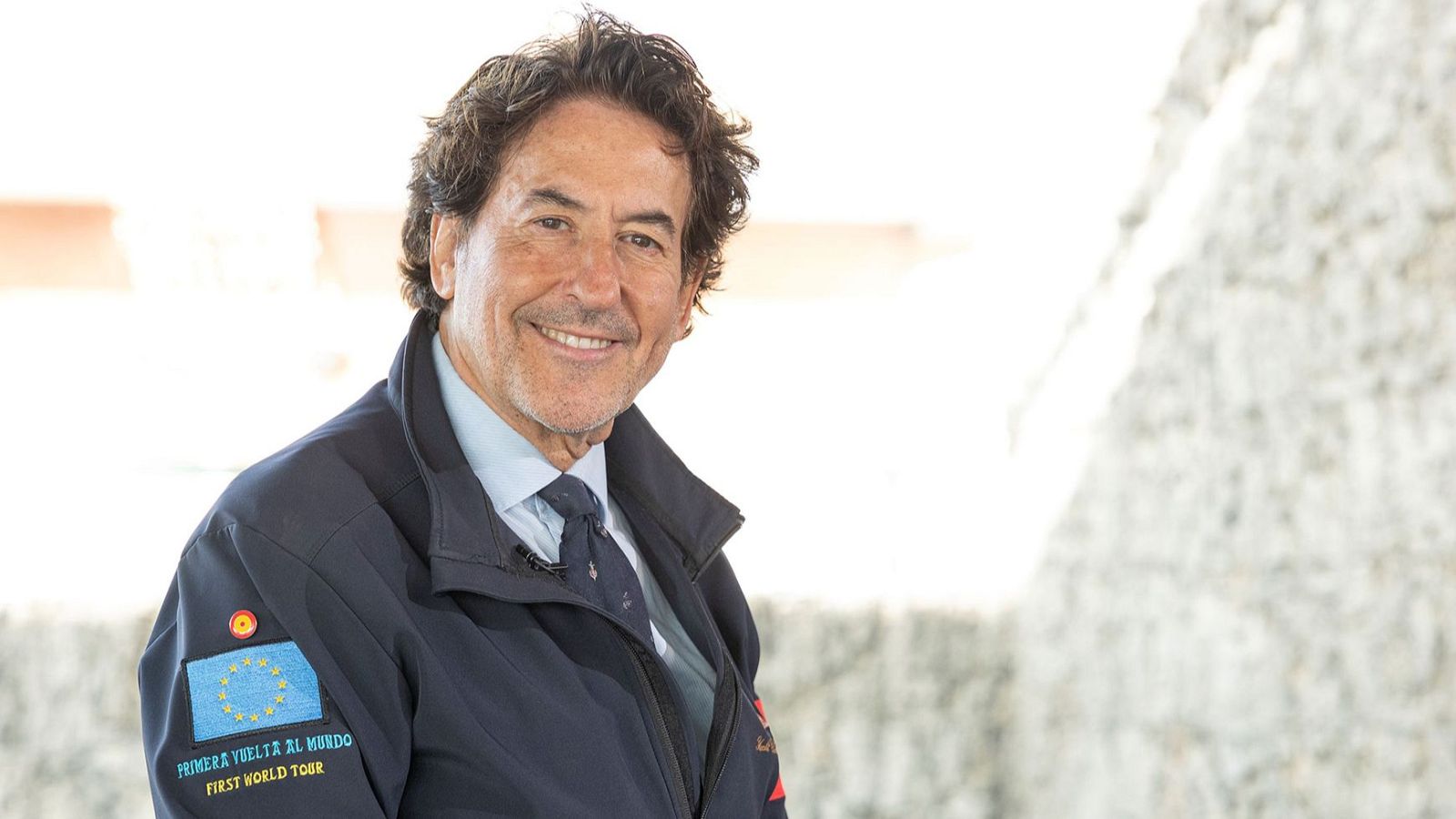 Retrato de Álvaro de Marichalar con chaqueta azul, luciendo parches de España y UE, y el texto "PRIMERA VUELTA AL MUNDO / FIRST WORLD TOUR".