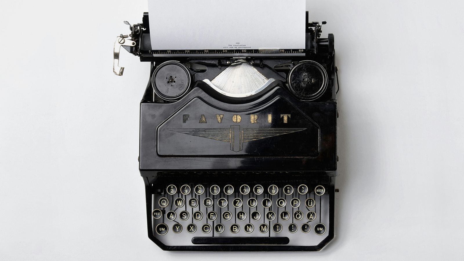 Máquina de escribir antigua "FAVORIT" negra y dorada, con teclado QWERTZ y papel insertado. Vista cenital sobre fondo blanco.