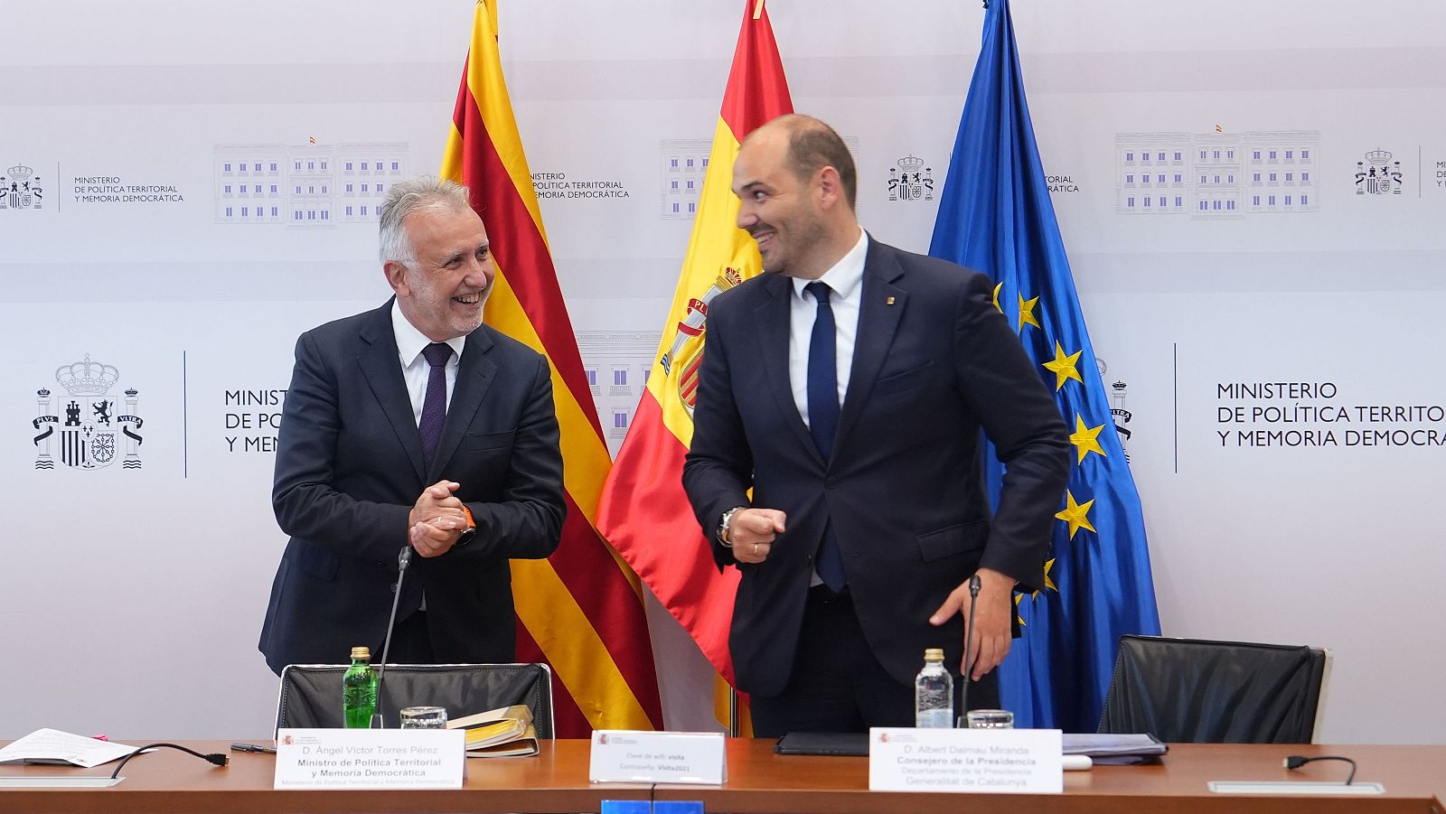 Dos hombres, Ángel Víctor Torres Pérez (Ministro) y Albert Dalmau Miranda (Conseller), sonríen en una reunión oficial frente a las banderas de Cataluña, España y la UE. Se lee "MINISTERIO DE POLÍTICA TERRITORIAL Y MEMORIA DEMOCRÁTICA".