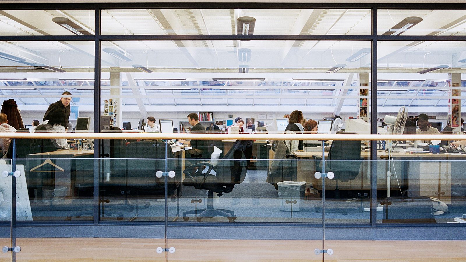 Vista panorámica de una oficina moderna con empleados trabajando, iluminada por luz natural y artificial. Se aprecian escritorios, ordenadores y mobiliario ergonómico.