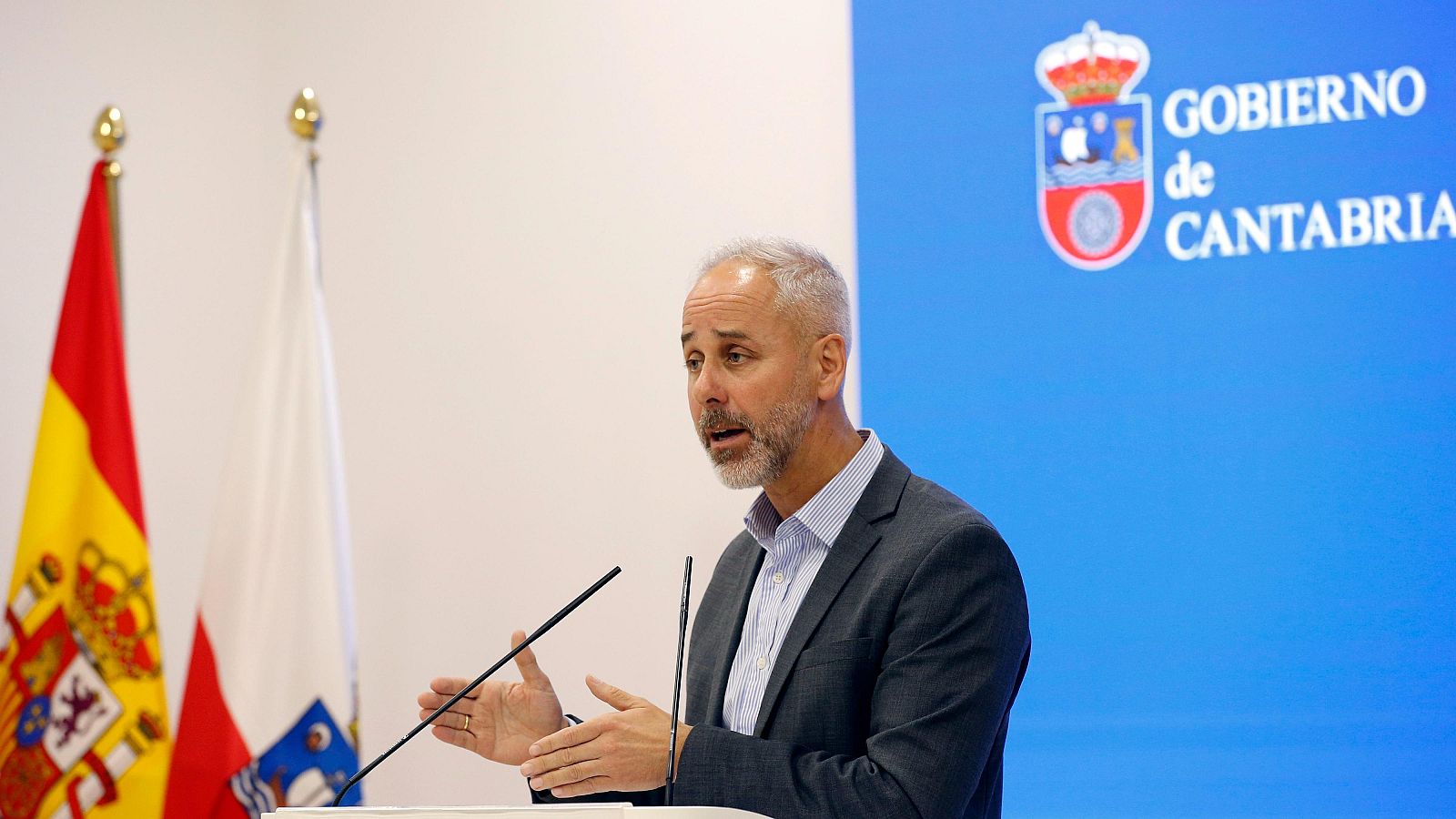 Sergio Silva, Consejero de Educación de Cantabria, habla en una rueda de prensa. Se observan las banderas de España y Cantabria, y el escudo del Gobierno de Cantabria al fondo.