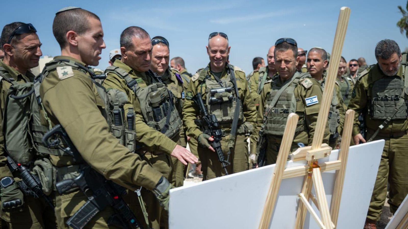 Eyal Zamir, jefe del Estado Mayor israelí, con uniforme militar y rifle, participa en una evaluación de situación en Cisjordania, donde otro soldado señala un panel informativo.