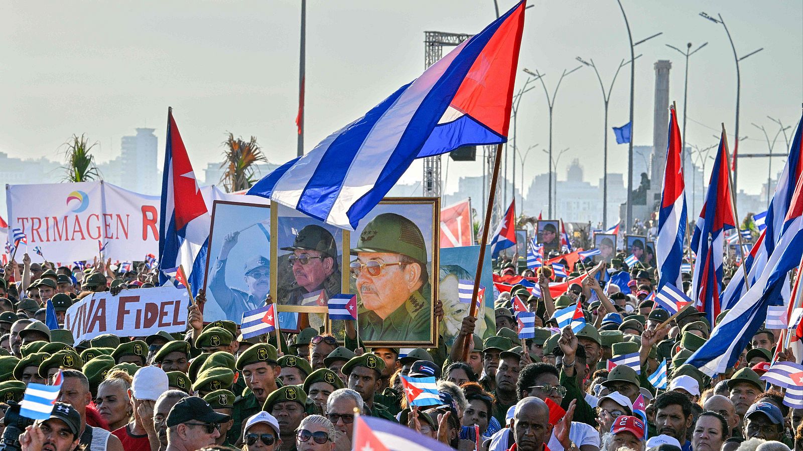 Multitud masiva en manifestación al aire libre con banderas cubanas y retratos de Fidel y Raúl Castro. Se aprecian gorras militares verdes y pancartas de apoyo a Fidel.