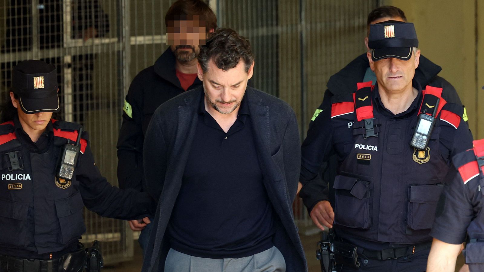 Jonathan Andic, escoltat per dos agents dels Mossos d'Esquadra, amb uniforme policial, a l'entrada d'un edifici oficial.