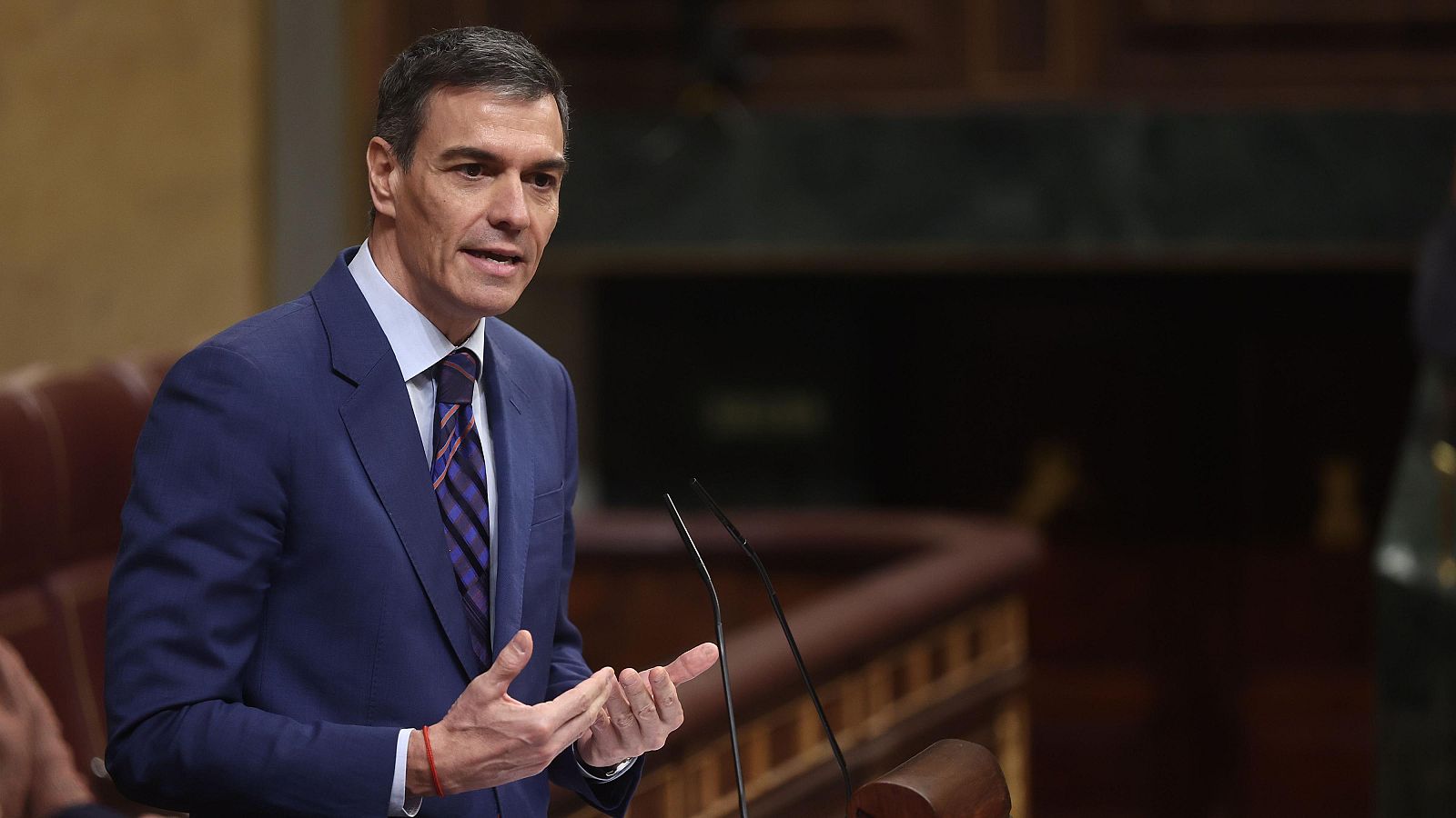 Pedro Sánchez, el presidente del gobierno, interviene en el Congreso de los Diputados, vistiendo traje oscuro y corbata a rayas, gesticulando frente a un atril con micrófonos.