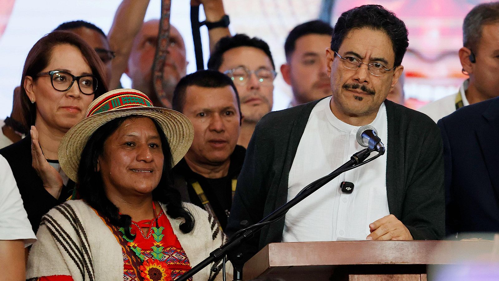 Iván Cépeda y Aida Quilcué en un evento público. Cépeda con gafas y barba, Quilcué con sombrero y poncho. Fondo con público.