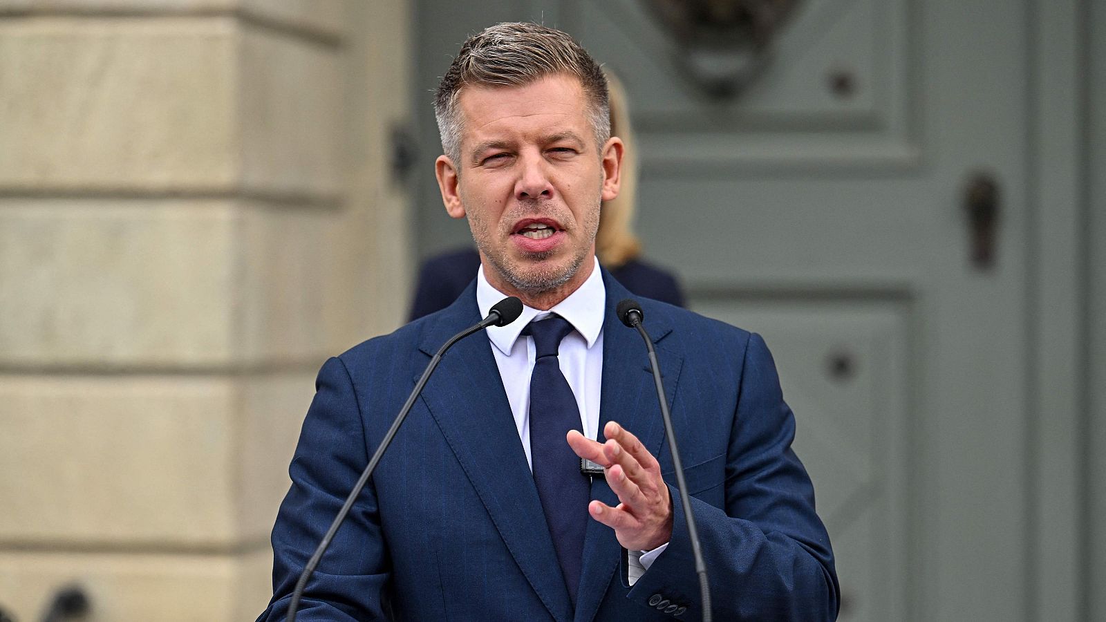 Peter Magyar, con traje azul marino y barba, habla en una rueda de prensa ante el Palacio Sandor en Budapest, con micrófonos y gesto comunicativo.