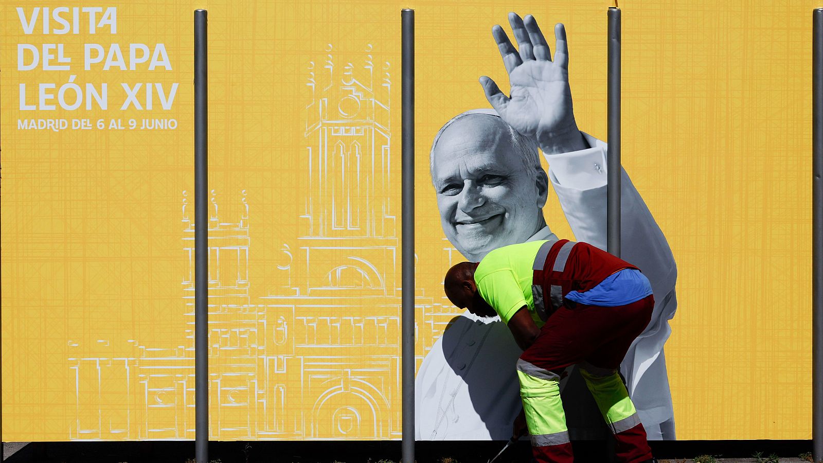 Valla publicitaria amarilla anuncia la visita del Papa León XIV a Madrid del 6 al 9 de junio, con imagen del Papa y un operario trabajando.
