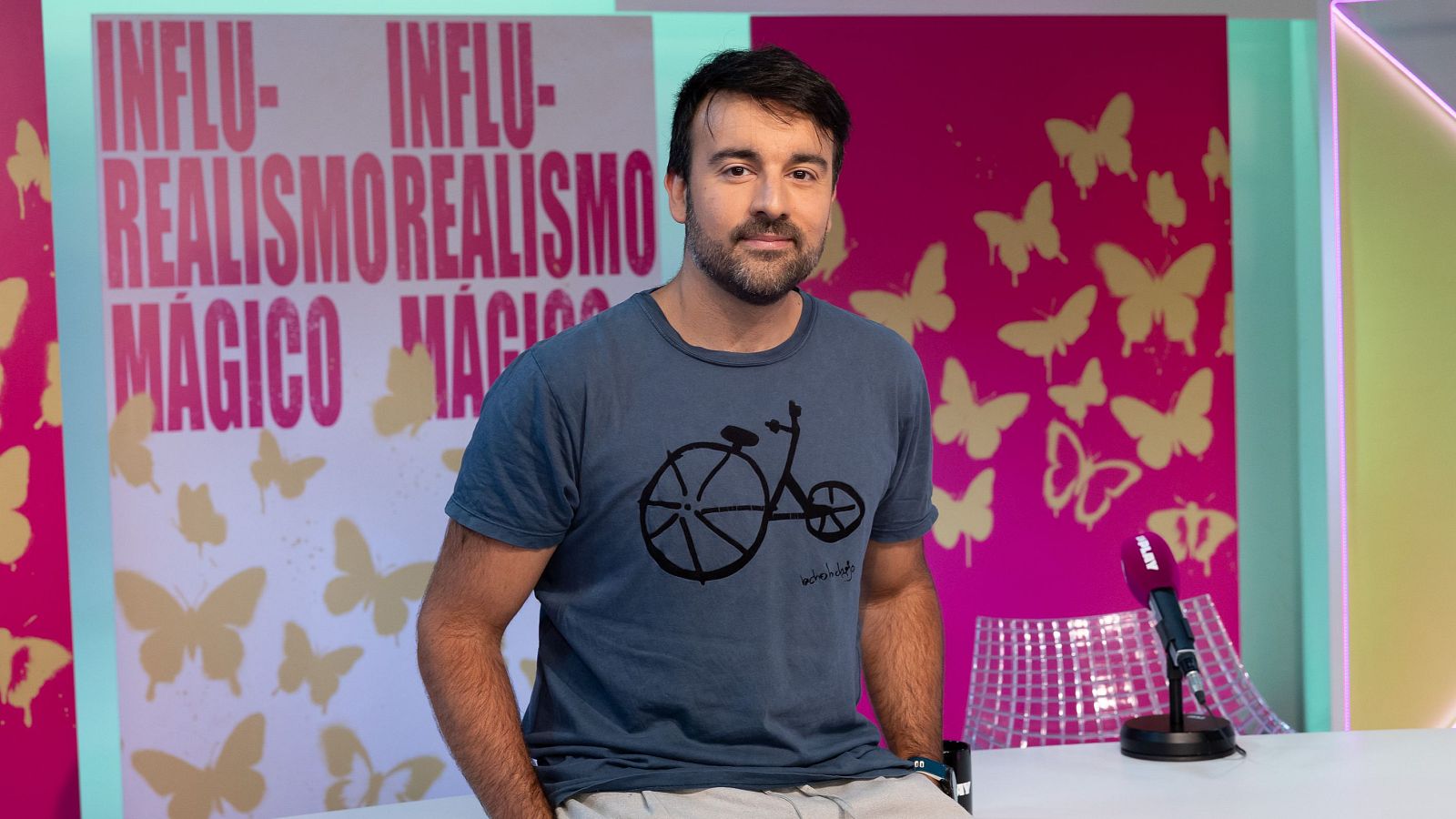 El divulgador Aitor Sánchez posa apoyado en la mesa de Influ-Realismo Mágico