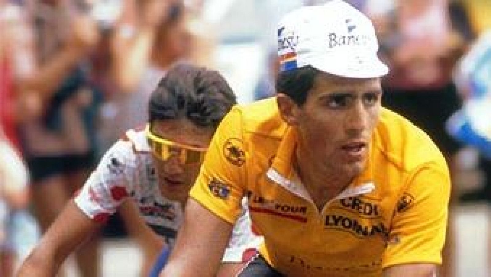 Miguel Induráin, con maillot amarillo "CREDIT LYONNAIS" "LE TOUR" y gorra "Banesto", compite en el Tour de Francia, mostrando concentración. Otro ciclista le sigue.