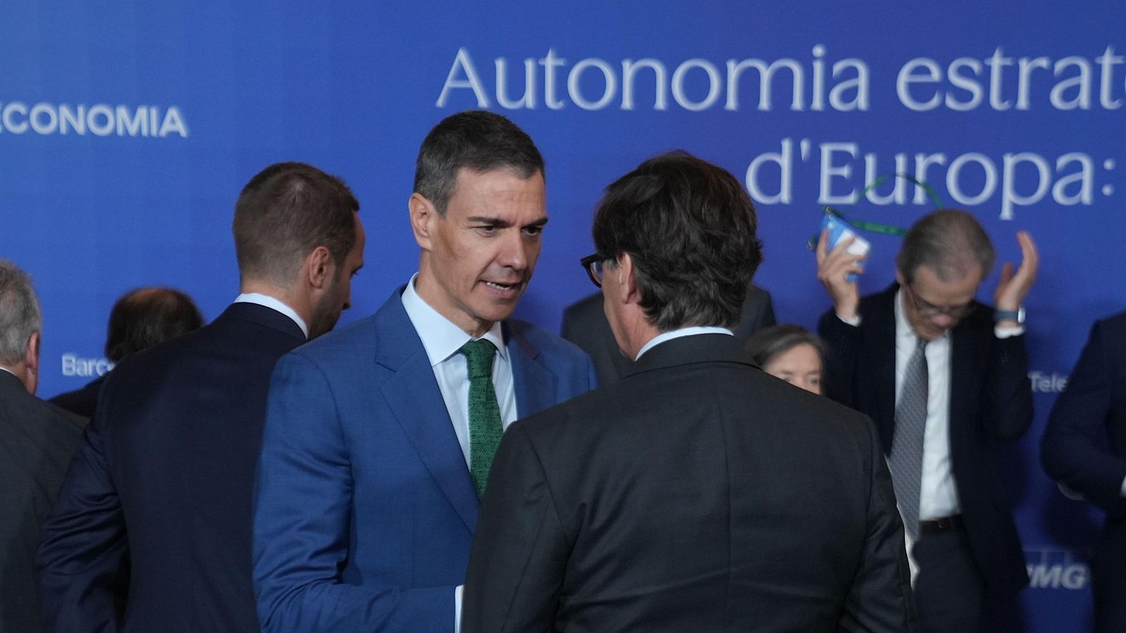 Pedro Sánchez conversa amb Salvador Illa al Cercle d'Economia. Sánchez (esq.) porta vestit blau i corbata verda; Illa (dret, d'esquena) porta vestit fosc i ulleres. Fons blau amb text "ECONOMIA".