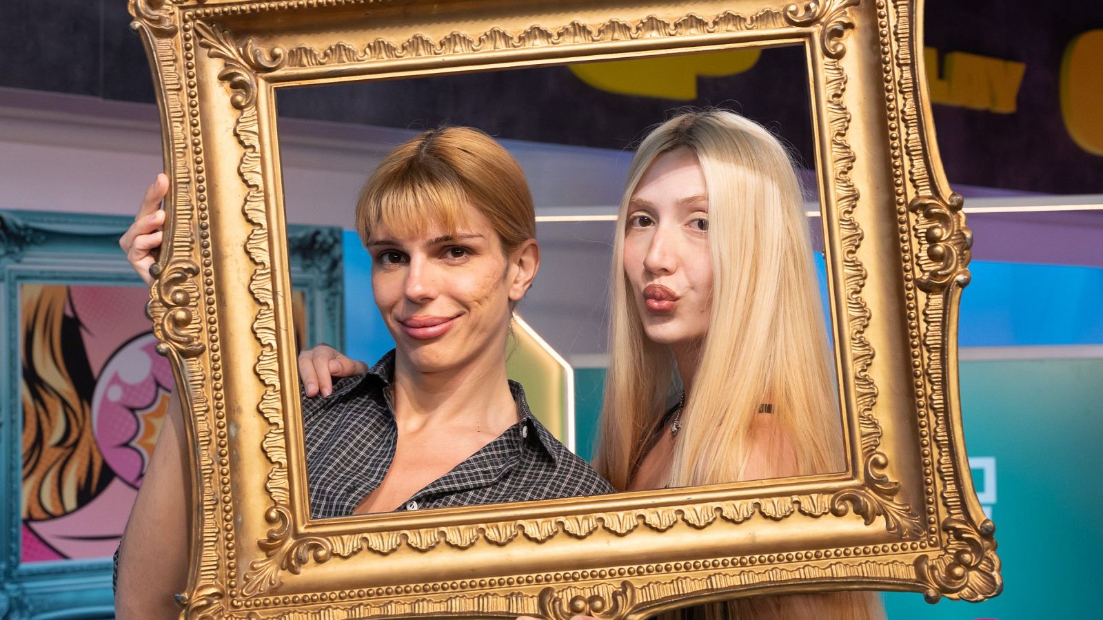 Samantha Hudson y María Barrier posan con un marco dorado, en un fondo colorido y abstracto, para el programa "¡Menudo Cuadro!".