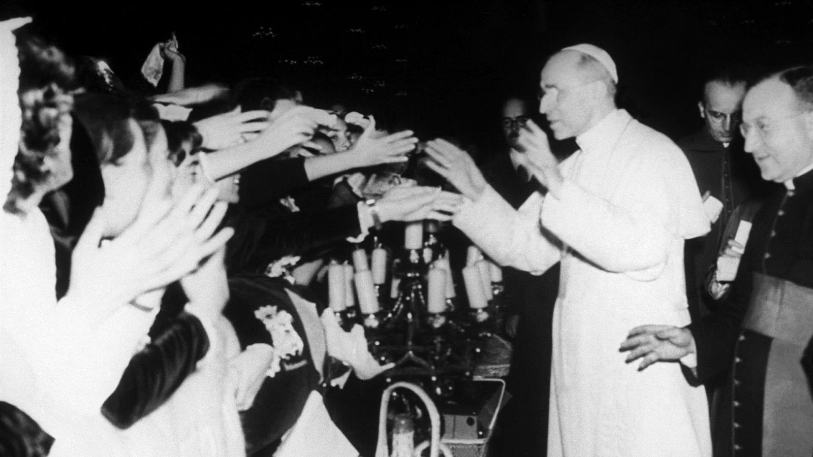 Papa Pío XII saluda a jóvenes españolas en el Vaticano en 1950. Detalle de un candelabro en primer plano. Fotografía histórica en blanco y negro.
