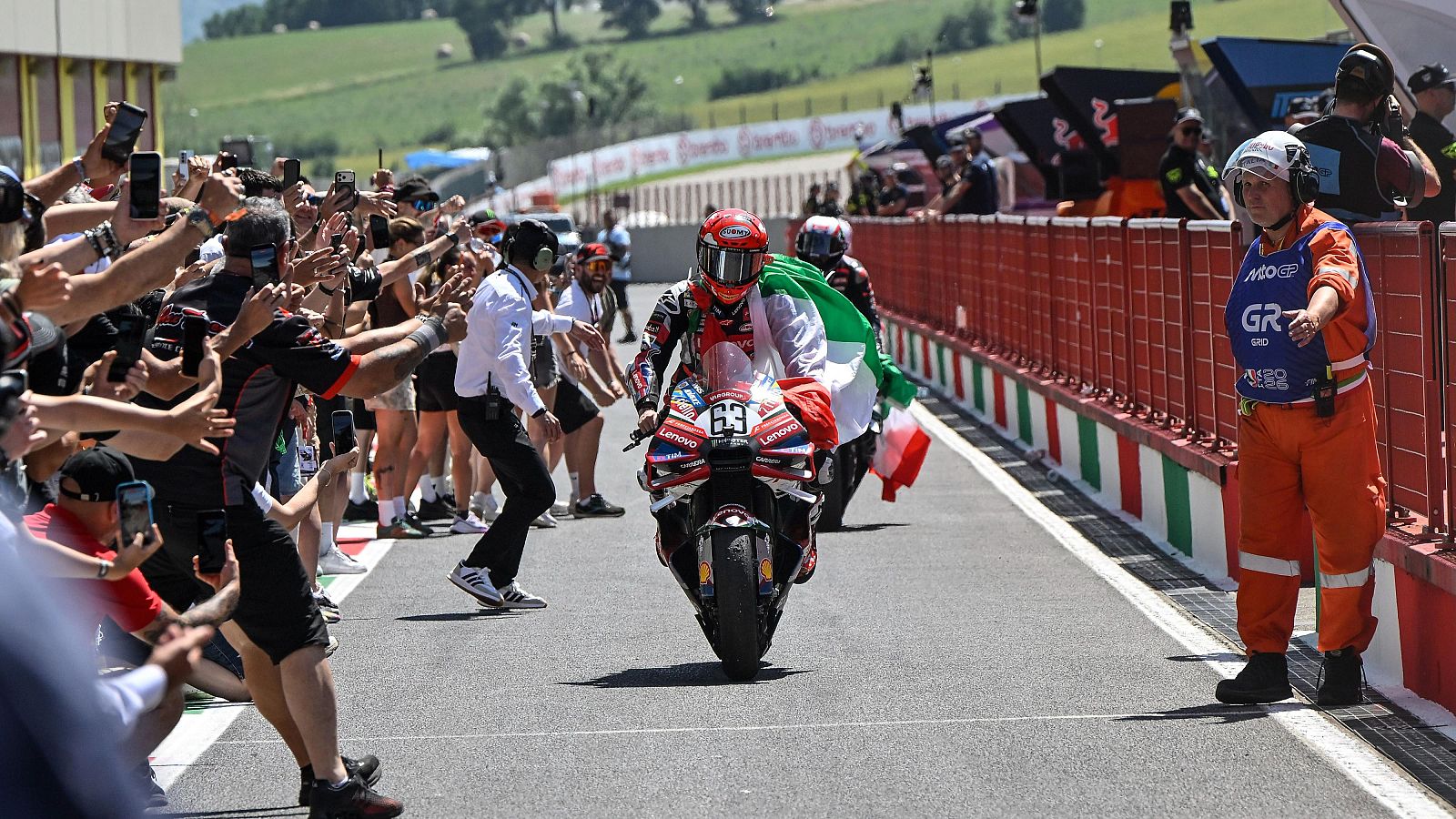 Francesco Bagnaia con el dorsal 63 celebra su podio en el GP de Italia de MotoGP 2026 a bordo de su Ducati Desmosedici, ondeando la bandera italiana ante una multitud.