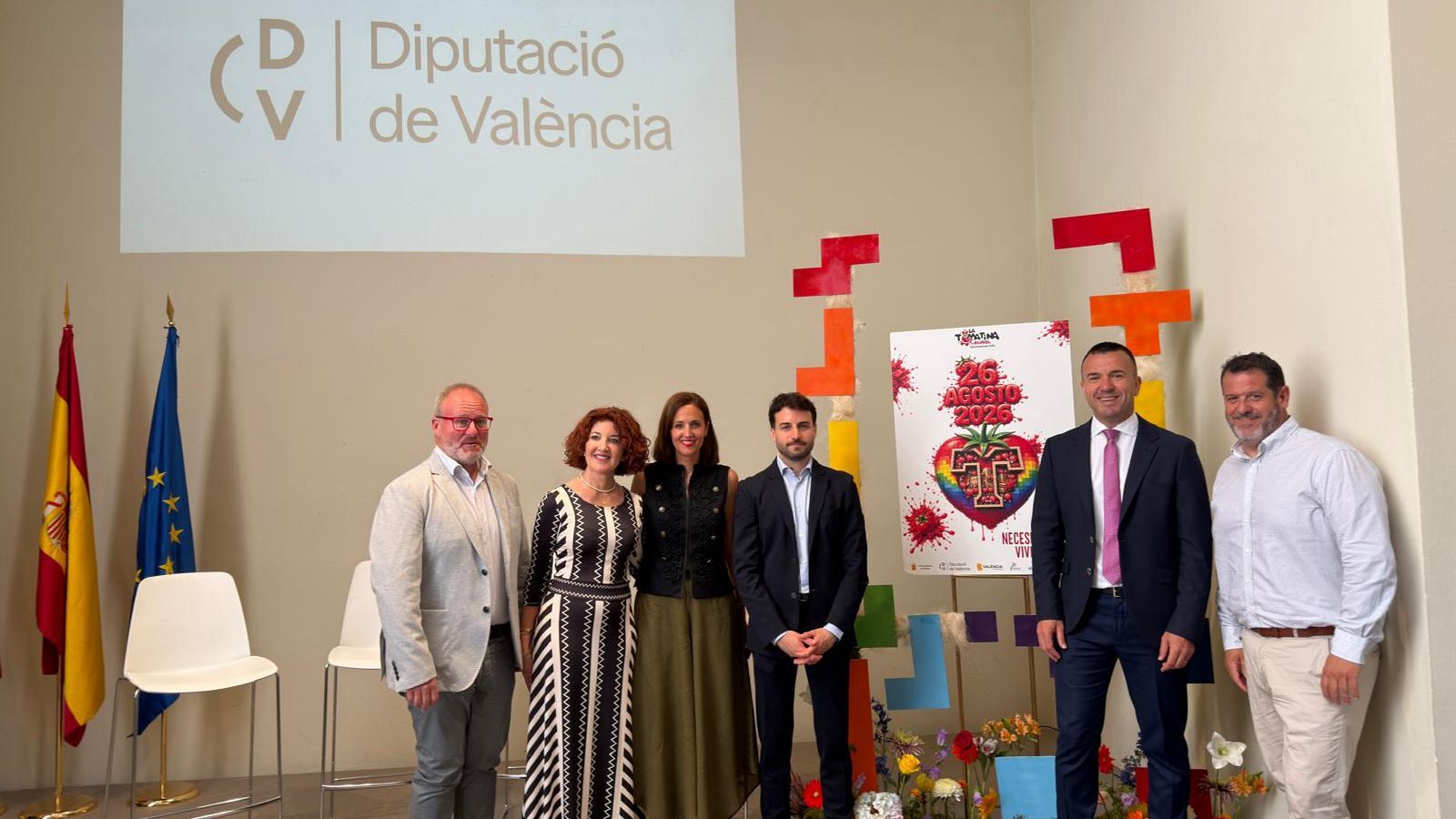 Seis personas posan en un evento oficial con banderas de España y UE, un cartel de "La Tomatina" y el logo de "Diputació de València".