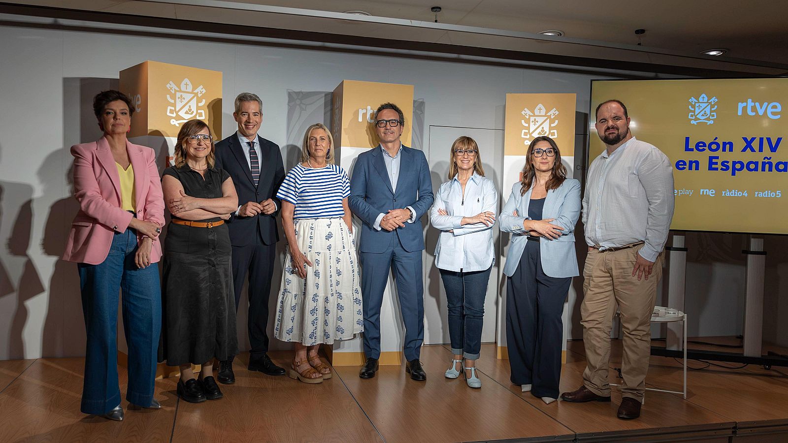 Ocho personas, incluyendo a Cristina Villanueva, Pilar Bernal, Oriol Nolis, Ana María Bordas, David Picazo, Gemma Nierga, Sonia Urbano y Jaime Gutiérrez, posan en un evento de RTVE. Una pantalla muestra "León XIV en España" y "play me radio5".