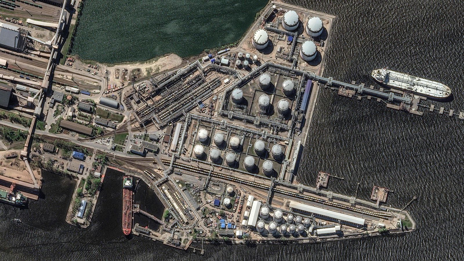 Terminal petrolera con tanques, tuberías, muelles, buques cisterna y vías férreas en una península.