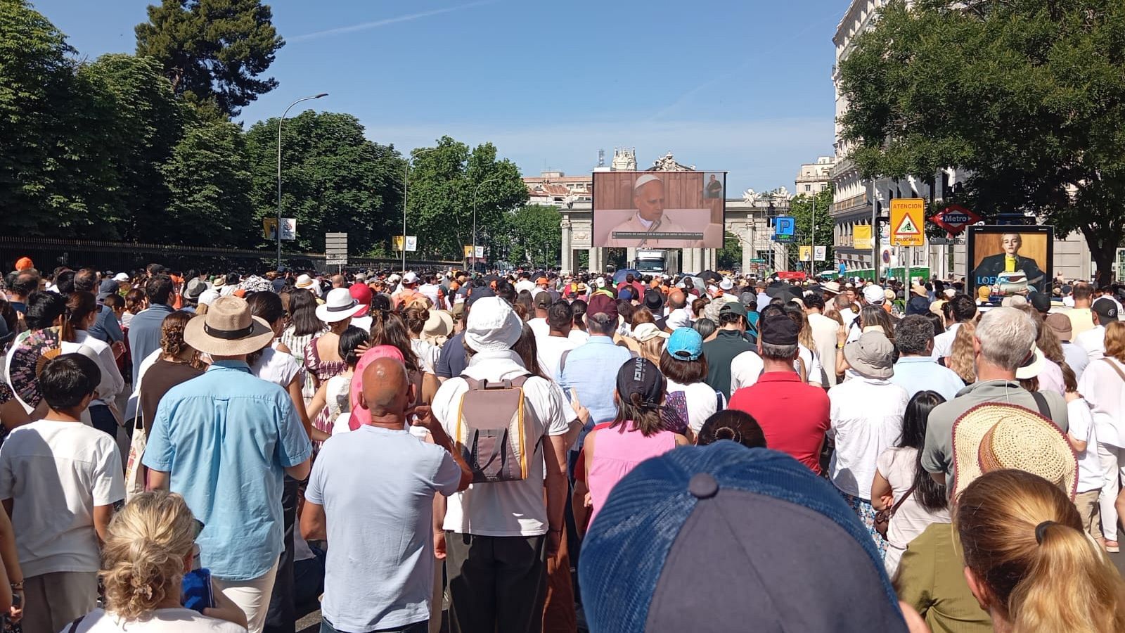 Miles de personas asisten a un evento al aire libre en Madrid, observando al Papa Francisco en una pantalla gigante, con la Puerta de Alcalá de fondo.