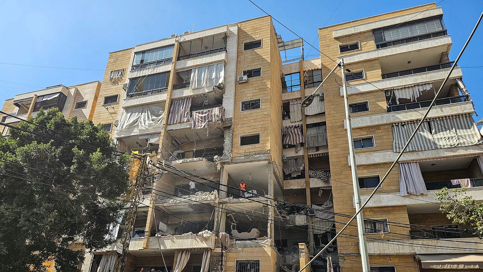 Edificio de apartamentos devastado por un ataque aéreo, con la sección central colapsada, interiores expuestos y personal de emergencia en la zona.