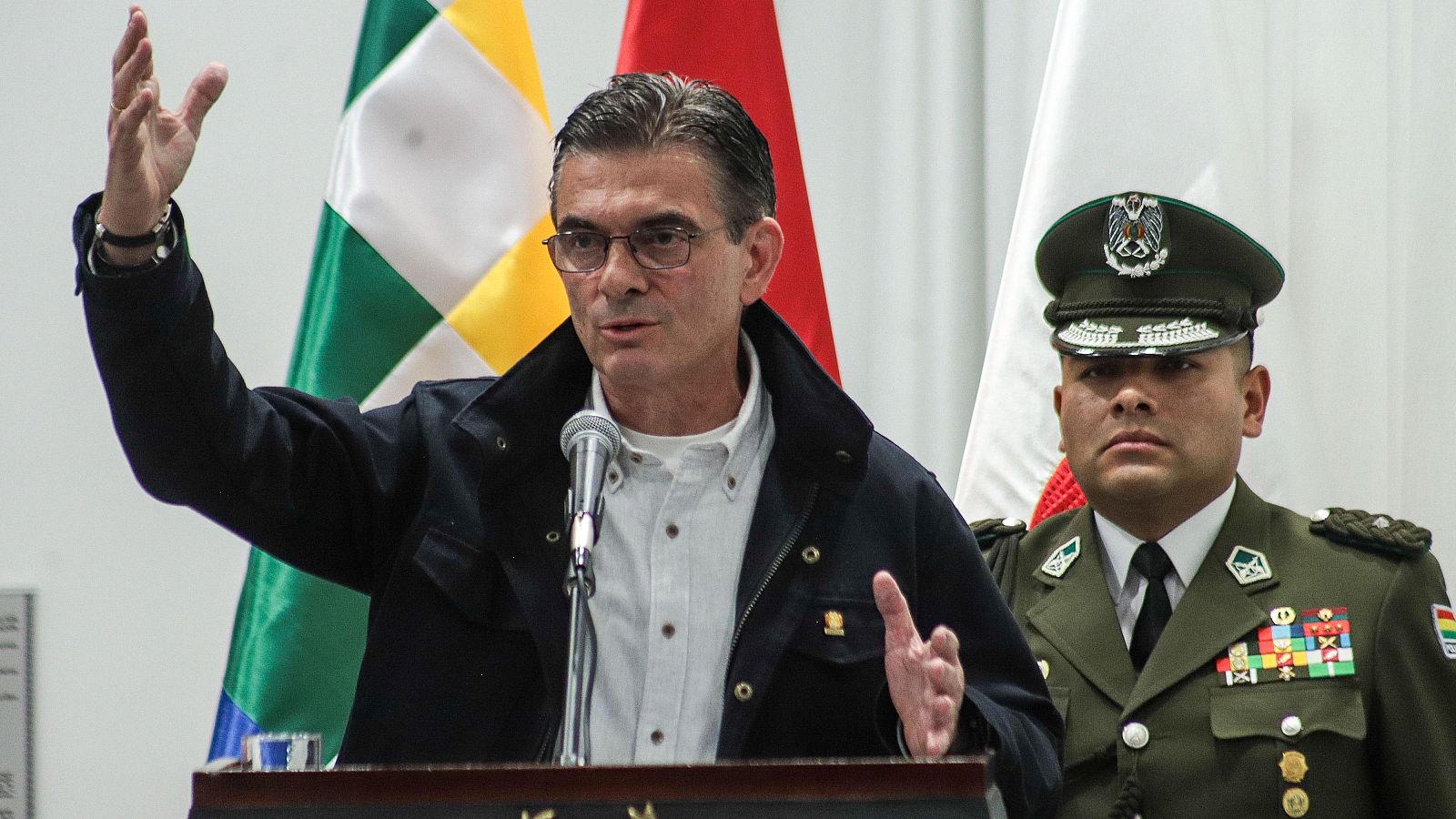 Rodrigo Paz, presidente de Bolivia, habla en un evento oficial, flanqueado por un oficial militar y banderas.