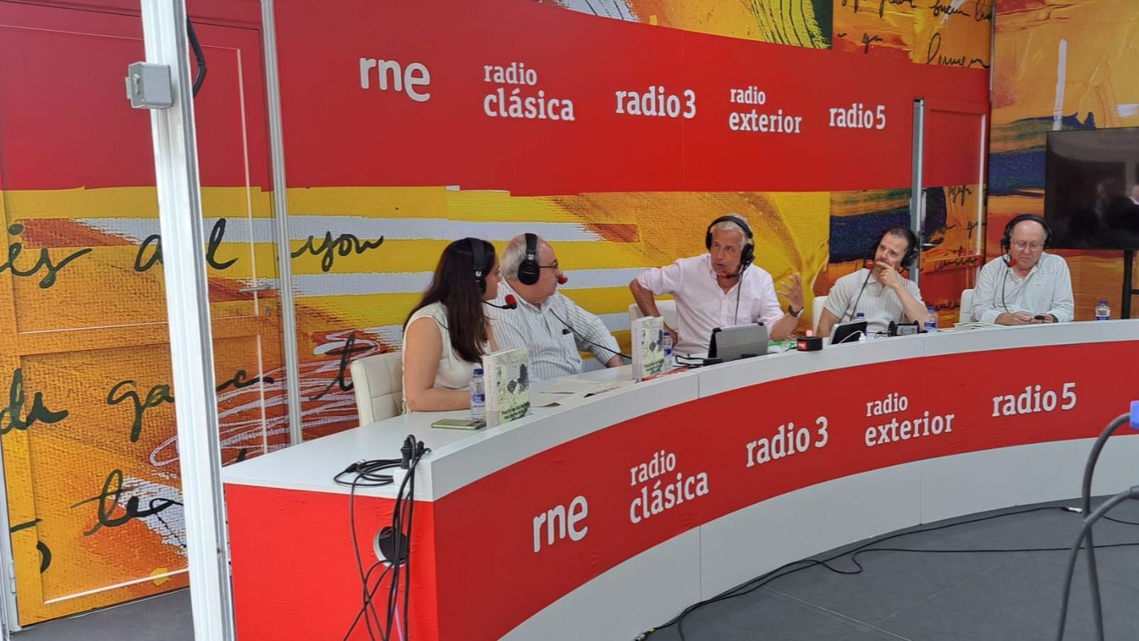 Cinco personas, incluyendo a Juan Carlos Ortega y Juan Ramón Lucas, participan en una emisión de radio desde un estudio de RNE, rodeados de equipo de audio y logos de la emisora.