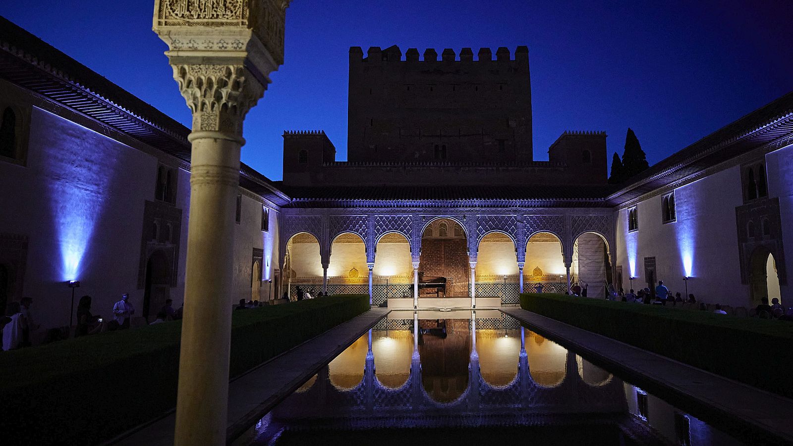 Vista nocturna del Patio de los Arrayanes en la Alhambra, con un estanque que refleja la arquería, columnas ornamentadas y la torre de Comares bajo un cielo estrellado.