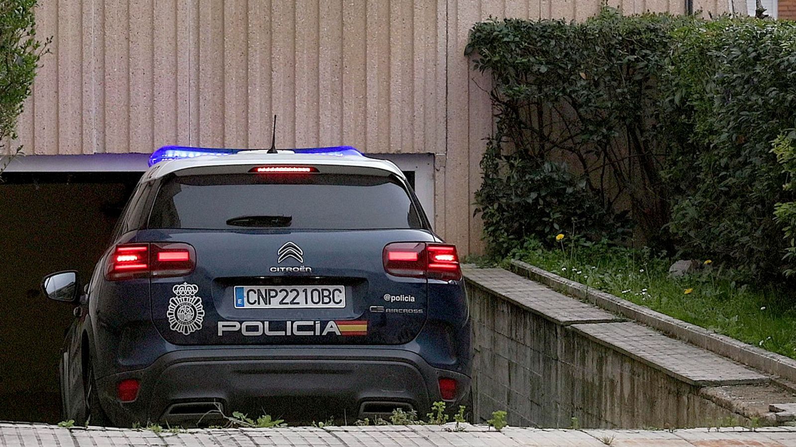 Vehículo policial Citroën C5 Aircross de la Policía Nacional de España, matrícula CNP2210BC, con luces de emergencia encendidas, estacionado en la entrada de un garaje.