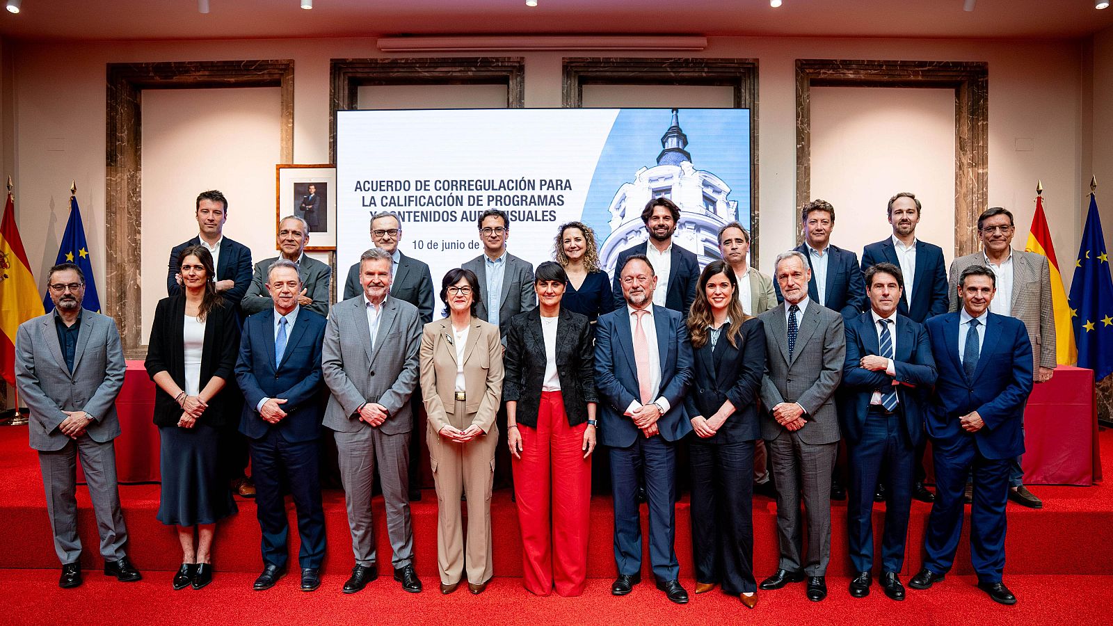 Fotografía de grupo formal de 19 personas en un evento institucional con pantalla de título "ACUERDO DE CORREGULACIÓN PARA LA CALIFICACIÓN DE PROGRAMAS Y CONTENIDOS AUDIOVISUALES" y fecha "10 de junio".