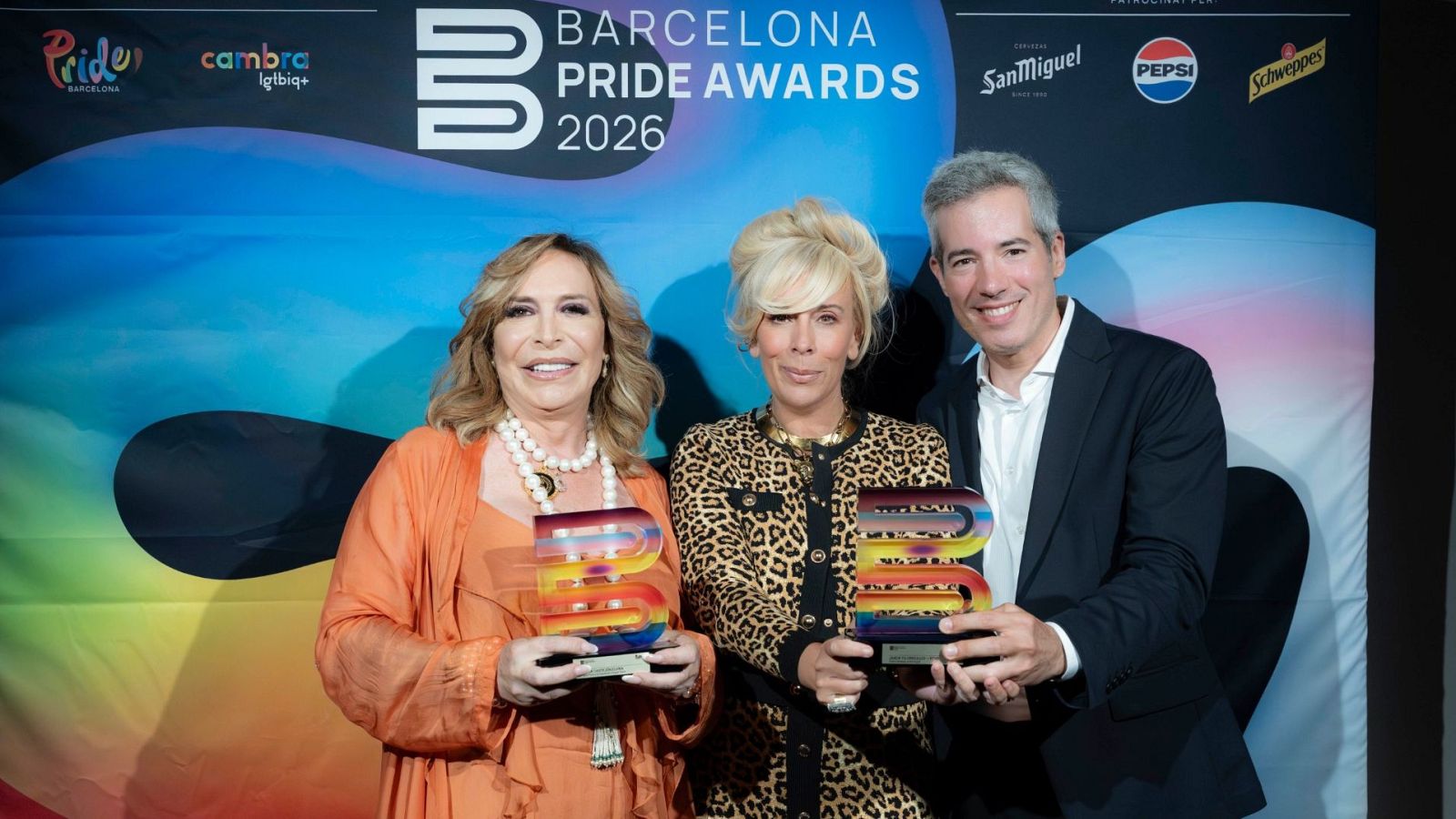 Benita Castejón, María Eizaguirre y Oriol Nolis celebran los Barcelona Pride Awards 2026, sosteniendo premios arcoíris frente a un panel con el nombre del evento y logos.