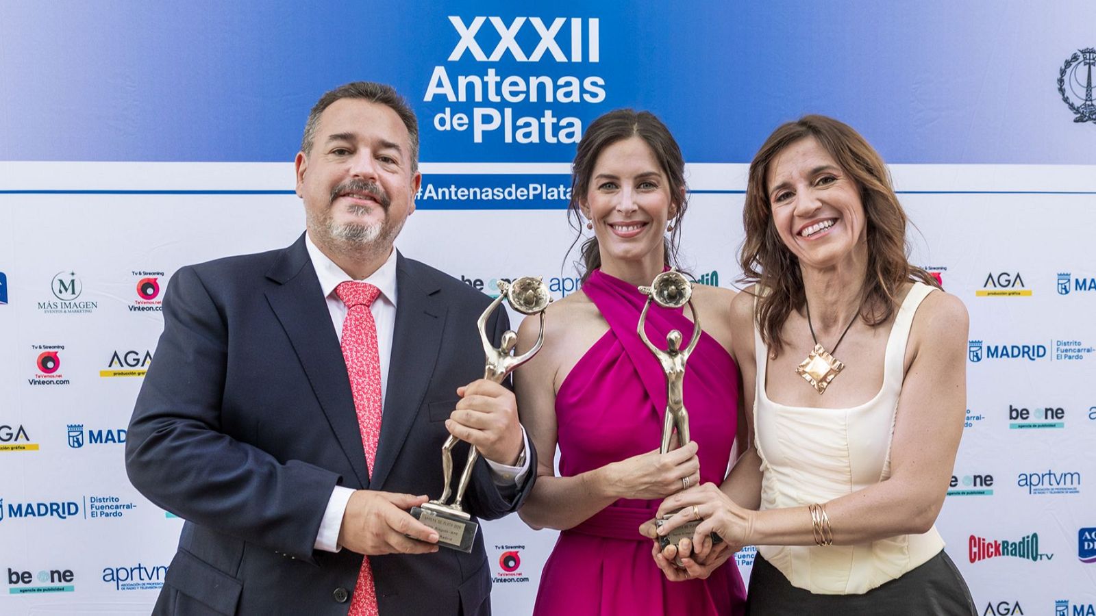Pablo Mingote, Paloma Soroa y Ana Marín Olmedo celebran su galardón en los XXXII Antenas de Plata, con trofeos y un fondo que destaca el evento y sus patrocinadores.