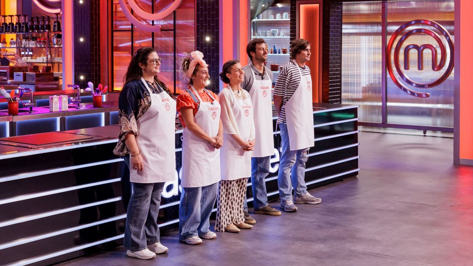 Cinco concursantes de MasterChef 14: Katherine, Carla, María, Gonzalo y Álvaro, posan en el set de cocina con sus delantales blancos. El logo de MasterChef es visible al fondo.