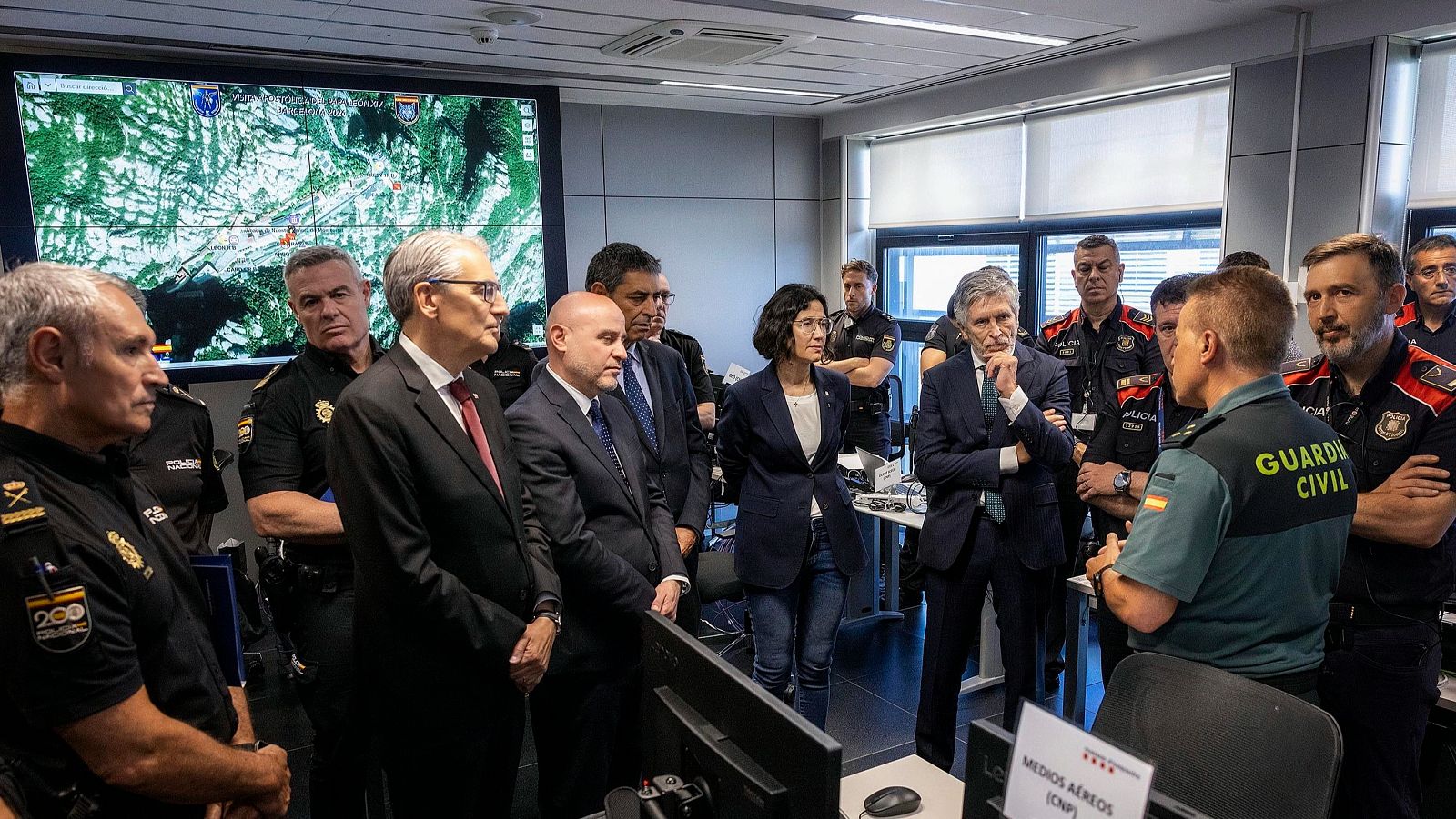 Reunión interinstitucional con Grande-Marlaska, Prieto y Parlon en una sala de control, mientras un agente de la Guardia Civil detalla información sobre medios aéreos del CNP.