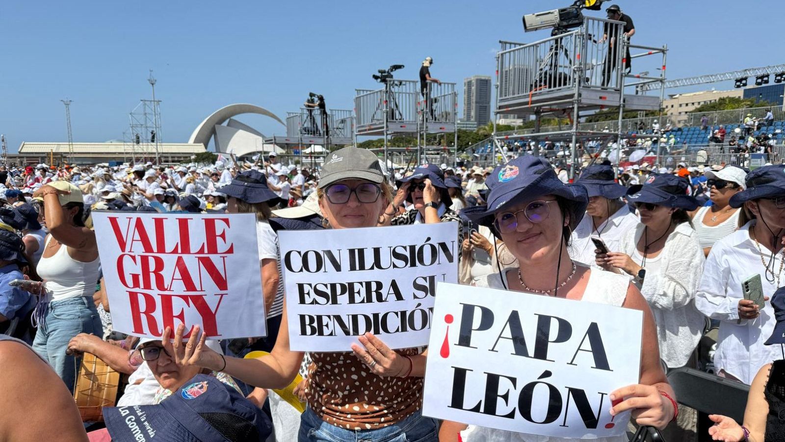 Un grupo de personas de La Gomera con carteles y banderas esperando el inicio de la misa del papa León XIV